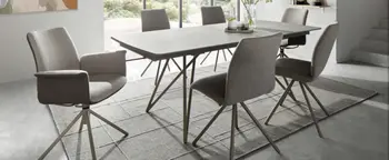 Esszimmer mit grauem Esstisch, vier Polsterstühlen und großem Teppich vor bodentiefen Fenstern und Treppe rechts.